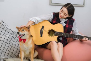 Güzel Asyalı kadın elinde gitarıyla kanepede oturuyor..