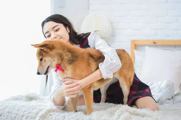 Beautiful asian woman\'s face lights up with joy as she plays with her furry companion on the bed.