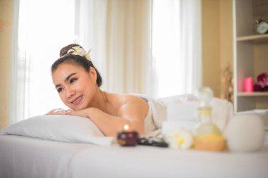 Güzel Asyalı kadın yan bakarken beyaz yatakta uzanıyor ve yanında bir bardak kaplıca yağı var..