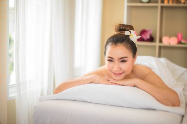 Güzel Asyalı kadın, elleri çenesinde, yüzünde gülümsemeyle rahat bir şekilde yatağında uzanıyor..