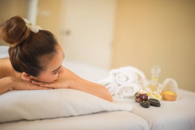 Güzel Asyalı kadın, spa yağına bakarken ellerini çenesinin üzerine koyup rahat bir şekilde yatağa uzanır..