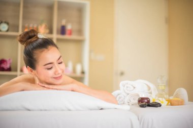 Güzel Asyalı kadın spa odasında uzanmış, mutlu bir gülümsemeyle kaplıca yağı şişesine bakıyor ve fotokopi çekiyor..