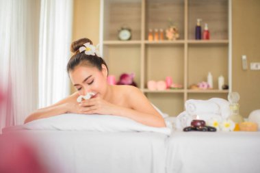 Güzel Asyalı kadın spa odasında beyaz yatağa uzanmış elinde bir buket kokulu beyaz Frangipani çiçeği tutuyordu..