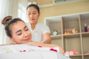 Güzel Asyalı müşteri, gül yapraklarıyla kaplı beyaz bir yatakta profesyonel bir masöz tarafından masaj yaptırmak konusunda rahat hissediyor..