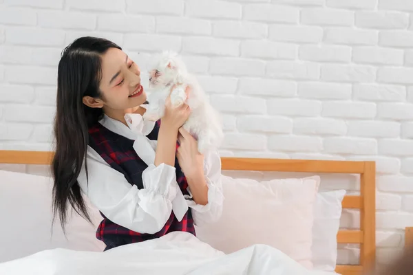 Beautiful asian woman\'s face lit up with delight as she holding the little white dog on the bed.