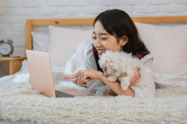 The beautiful asian girl was pointing at the laptop screen showing her little white dog something interesting.