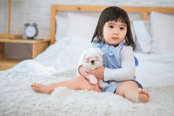 The little girl\'s eyes shone with joy as she held the fluffy white dog on the bed in the cozy bedroom.