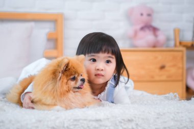 Yüzünde bir gülümsemeyle küçük kız yan tarafa bakıyordu. Belki de düşünceye dalmıştı. Ya da yatakta sevimli köpeğiyle anın tadını çıkarıyordu..