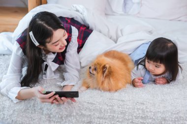 Güzel Asyalı kız elinde telefonla yatak odasında yatan köpeğe ve küçük kıza resim gösteriyor.