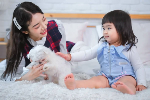 As they played the little girl and beautiful asian woman exchanged loving glances grateful for each other\'s company and the joy their furry friend brought into their lives.