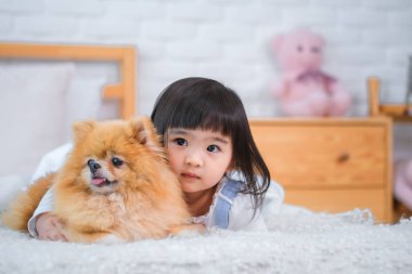 Küçük kız, yatak odasında yanında uzanan köpeğe doğru eğildi ve kameraya baktı..