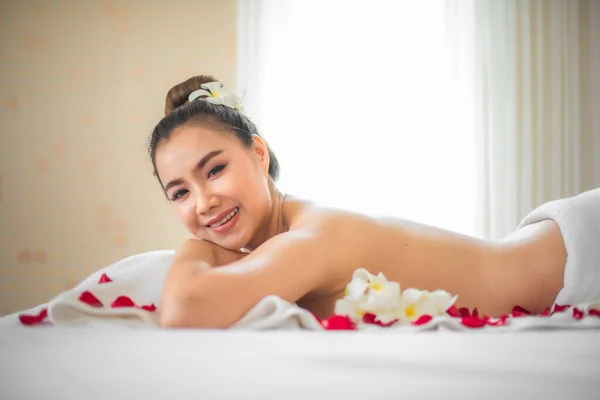 침대에 아름다운 아시아 여인을 둘러싸고 꽃잎은 순간의 과덧없는 특성을 상징하였다 — 스톡 사진