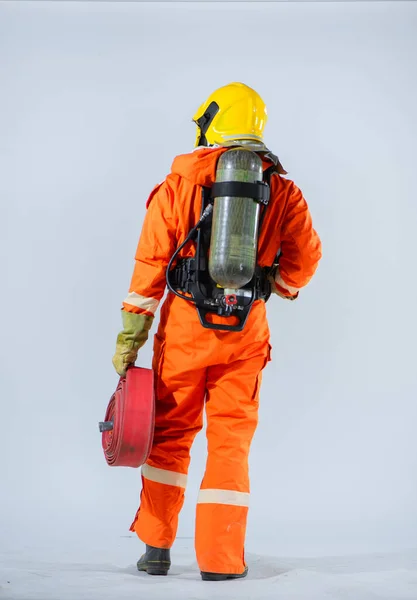白い背景に火のホースを保持しながら 黄色のヘルメットを身に着けている消防士の垂直写真は 彼の背中と立っている — ストック写真