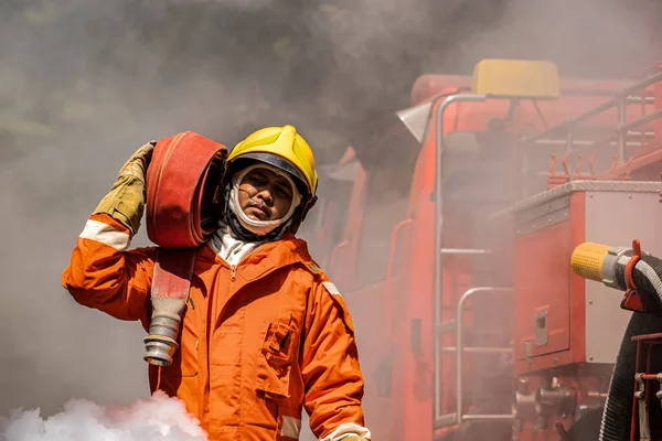 濃い煙と激しい熱にもかかわらず 消防士は不動の決意で肩に火のホースを運びます — ストック写真