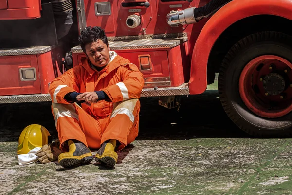 激しい救助活動から排出された消防士は 消防車にもたれて一瞬の休息を見つける彼の眠った姿勢で明らかに彼の疲労の重さ — ストック写真