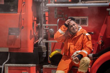 Yorgun bir ifade ve is lekeli kıyafetle itfaiyeci yoğun itfaiye çabalarını ve yangından etkilenen hayatları yansıtıyor..