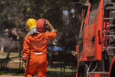 İtfaiyeci, itfaiye aracının yanında duruyor. Omuzlarında yangın hortumunu tutuyor. Kurbanlara yardım etmeye hazır..
