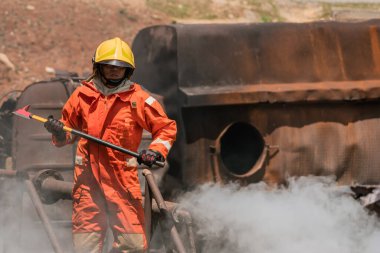 Sarı kask takan bir itfaiyeci elinde dumanla çevrili demir bir balta tutuyor..