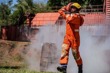 Profesyonel itfaiyeci, güvenli ve cesurca dumanın içinde yürüyor. Omuzunda bir yangın hortumu tutuyor..
