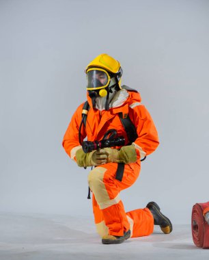 Profesyonel itfaiyeci sırtına oksijen tüpü takmış, yan bakıyor ve beyaz arka planda yangın hortumu tutuyor..