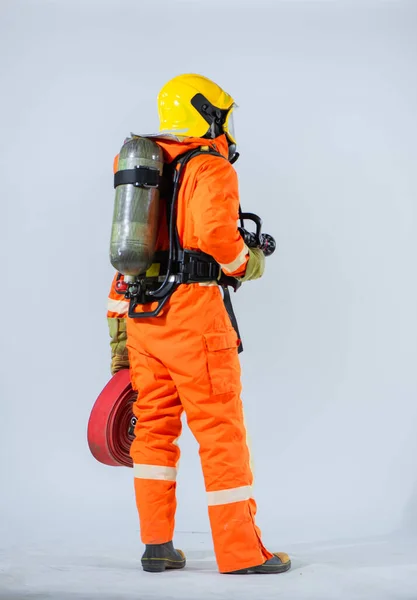 白い背景を横に見ながら プロの消防士は彼の背中に火のホースを保持し 彼の背中に酸素タンクを身に着けているオフに立っている — ストック写真