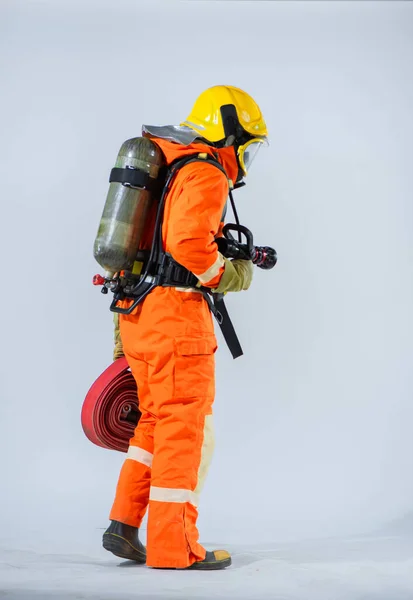 白地に床を見下ろしながら プロの消防士は 彼の背中に火のホースを保持し 彼の背中に酸素タンクを身に着けているオフに立っている — ストック写真