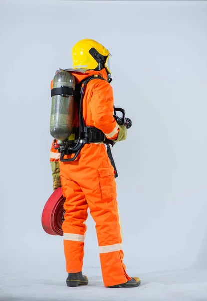 白地に酸素タンクを背にしながら プロの消防士が立って消防ホースを保持する垂直写真 — ストック写真