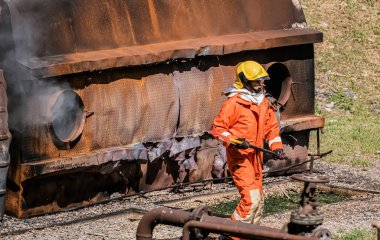 Demir baltayı sıkıca kavrayan itfaiyeci, hızlı hareket ve korunmaya olan bağlılıklarını simgeleyen özgüven ve hazırlık saçar..