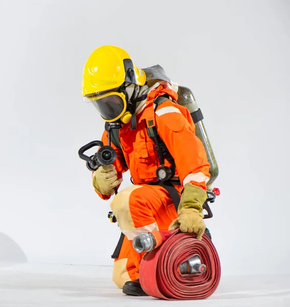 白い背景に酸素タンクを身に着けている間 プロの消防士は 座っている 横に膝を下に向け 火のホースを保持 — ストック写真