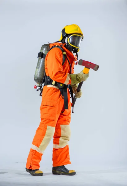 黄色いヘルメットをかぶったプロの消防士が 白地に酸素タンクを背負った鉄斧を背負ったまま横に立っている — ストック写真