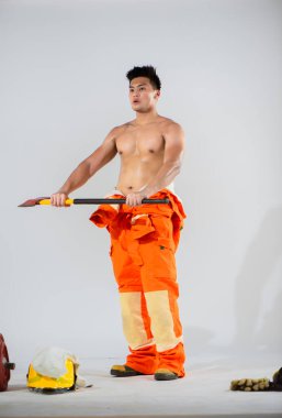 Yandan bakıldığında profesyonel itfaiyeci üstsüz duruyor ve iki eliyle demir bir balta tutuyor ve insanları kurtarıyor..