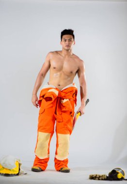 Üstsüz profesyonel itfaiyeci ayakta duruyor ve güçlü bir fiziksel güç ve ortaya çıkabilecek her türlü itfaiye mücadelesine hazır olma hissi yayıyor..