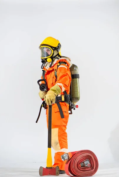 消防士の側面図は 地面に鉄斧を使用して白い背景に立っており 一方で消防ホースを持ち もう一方で背中の後ろに酸素タンクを持っている — ストック写真