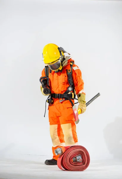 黄色の硬い帽子をかぶった消防士が白い背景に立っている一方で 彼は火のホースを保持し 一方で彼は鉄斧をつかむ — ストック写真