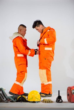 Profesyonel itfaiyeci, fermuarlarını titizlikle hizalamak için partnerini destekliyor. Böylece rahat ve güvenli bir ortama uyum sağlıyor..