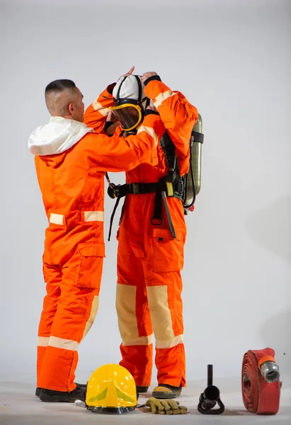 プロの消防士は慎重に安全と義務の行に保護の重要性を強調彼のパートナーの顔に適切なフィットを確保するためにマスクを調整します — ストック写真