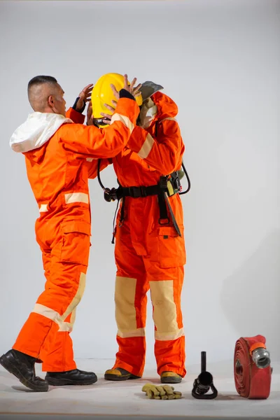 プロの消防士は白い背景に黄色のハード帽子をかぶっている彼のパートナーを助けています — ストック写真