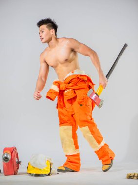 İtfaiyeci beyaz arka planda demir baltayı tutarken hazırlık pozisyonunda duruyor..