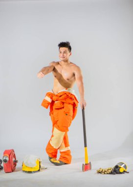 Üstsüz profesyonel itfaiyeci elinde demir baltayla zemini desteklerken beyaz bir arka planda yüzünde bir gülümsemeyle elini öne uzatıyor..