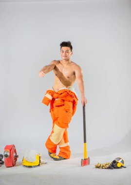 Profesyonel itfaiyeci elinde demir bir baltayla zemini desteklerken yüzünü gülümseterek beyaz arka planda elini öne doğru uzatıyor..