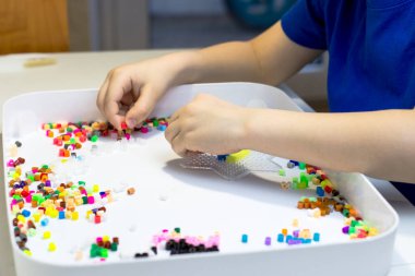 Bir çocuk termo mozaik çalıyor. Beyaz masada oynayan bir çocuk.