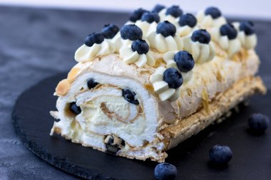 Koyu arkaplanda kremalı pasta rulosu. Yaban mersinli tatlı