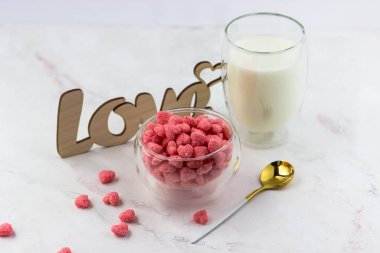 Bir kase kahvaltı gevreği, bir bardak süt ve beyaz bir masaya yazılmış ahşap bir aşk yazısı. Romantik kahvaltı.