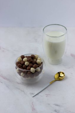 Beyaz arka planda vanilyalı ve çikolata toplu bir kase. Atıştırmalık ve bir bardak süt - hızlı kahvaltı