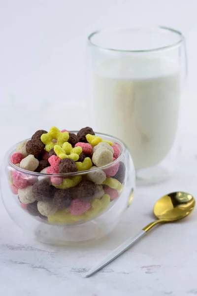 A bowl of snacks in the shape of a ball, hearts and flowers on a white marble table. Breakfast cereal and a glass of milk