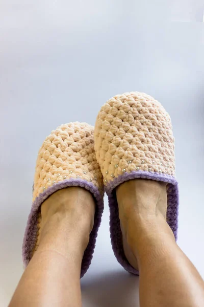 Women\'s legs in knitted peach-colored slippers. Needlework, knitting, home comfort