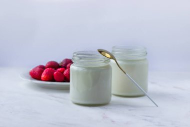 Ev yapımı yoğurt. Beyaz bir masada kavanozlar dolusu yoğurt ve çilek. Uygun beslenme