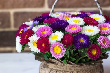 Sepet şeklinde bir buket küçük kasımpatı. Beyaz bir masanın üzerinde, tuğla bir duvarın karşısında.