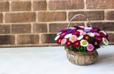 Sepet şeklinde bir buket küçük kasımpatı. Beyaz bir masanın üzerinde, tuğla bir duvarın karşısında.