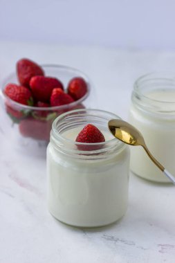 Ev yapımı yoğurt. Beyaz bir masada kavanozlar dolusu yoğurt ve çilek. Uygun beslenme
